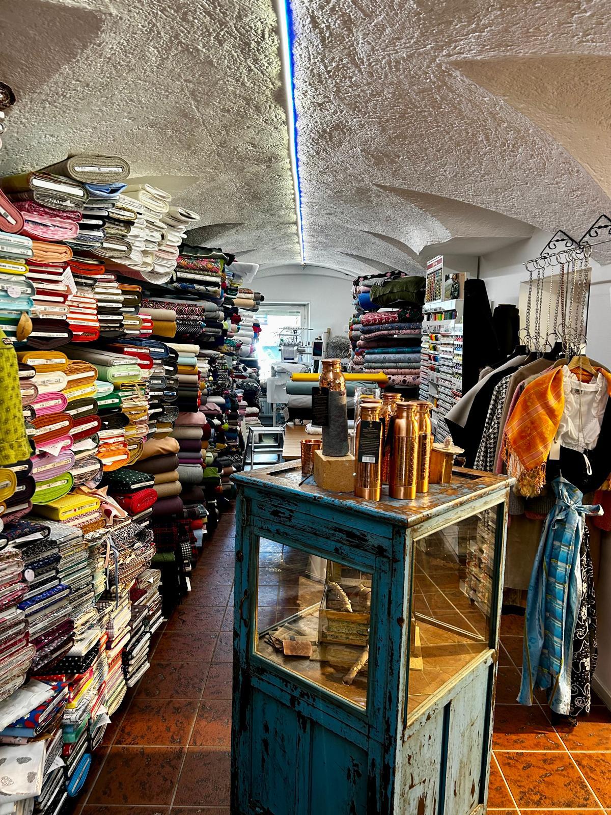 Impression aus Der Laden Aichach: farbige Stoffregale, eine vintage türkise Vitrine und Accessoires im lichtdurchfluteten Verkaufsraum